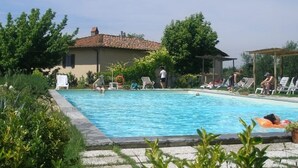 A swimming pool surrounded by greenery and a building with a tiled roof.