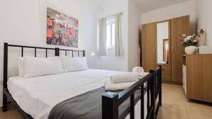 A bedroom with a bed, a wooden wardrobe, a mirror, and a window with curtains. - Modern 1-bedroom apartment ideally located near Balluta Bay and Sliema’s promenade. Includes a sofa bed, full kitchen, Wi-Fi, and A/C — everything you need for a comfortable stay close to shops, beaches, and restaurants. (Tas-Sliema)
