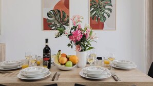 A dining table set with plates, glasses, a bottle of wine, a bowl of fruit, and a vase of flowers.