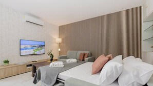 A modern hotel room with a bed, a sofa, a TV, and a wall-mounted air conditioner.