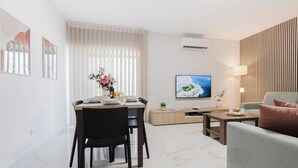 A modern living room with a dining area, a flat-screen TV mounted on the wall, and a wooden panel wall.