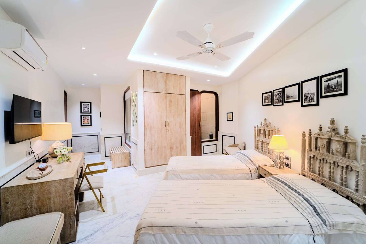 A modern bedroom with a large bed, bedside tables, a desk with a lamp, a wardrobe, and a ceiling fan.