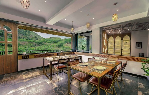 Un comedor con vistas a un follaje exuberante, una mesa de madera dispuesta con platos y sillas, y lámparas colgantes.