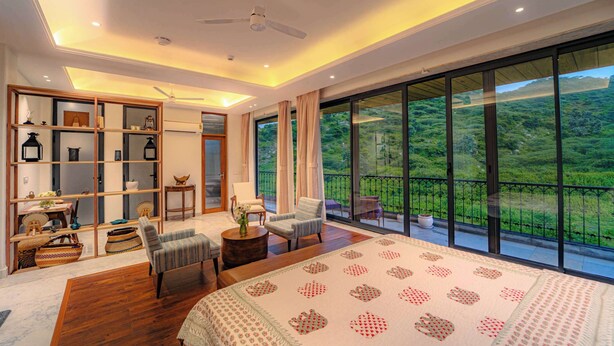 A spacious bedroom with a large bed, a seating area with chairs, a wooden floor, a built-in bookshelf, and a balcony with a scenic view. - Artisav House-A Luxury Boutique Stay (Amer)
