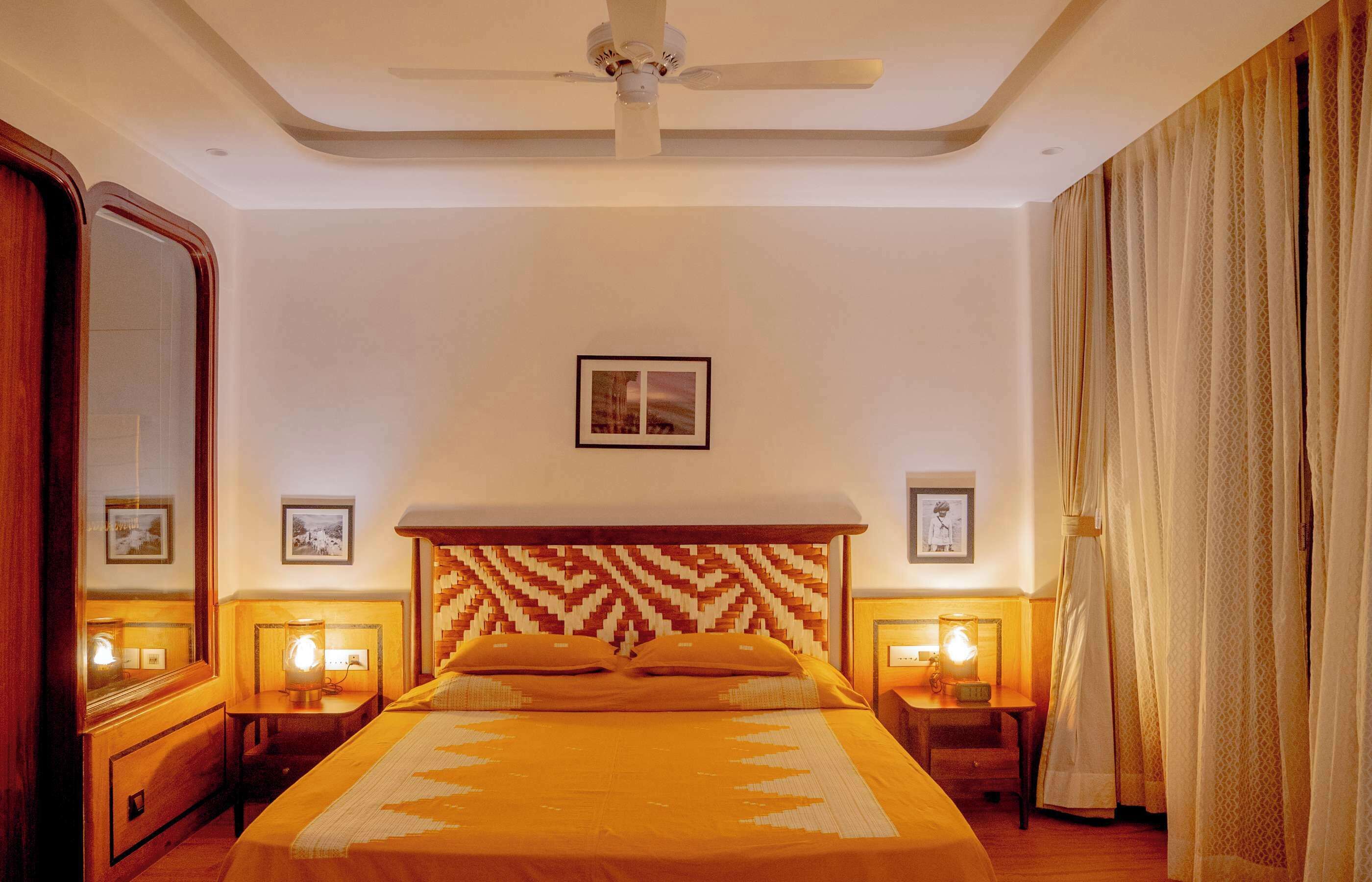 Une chambre d’hôtel avec un lit, des tables de chevet, un ventilateur de plafond et une grande fenêtre avec des rideaux.