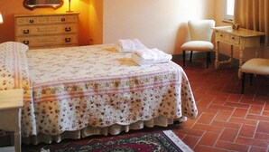 Une chambre à coucher comprenant un lit, une commode, une chaise, un bureau, un miroir et un luminaire fixé au mur.