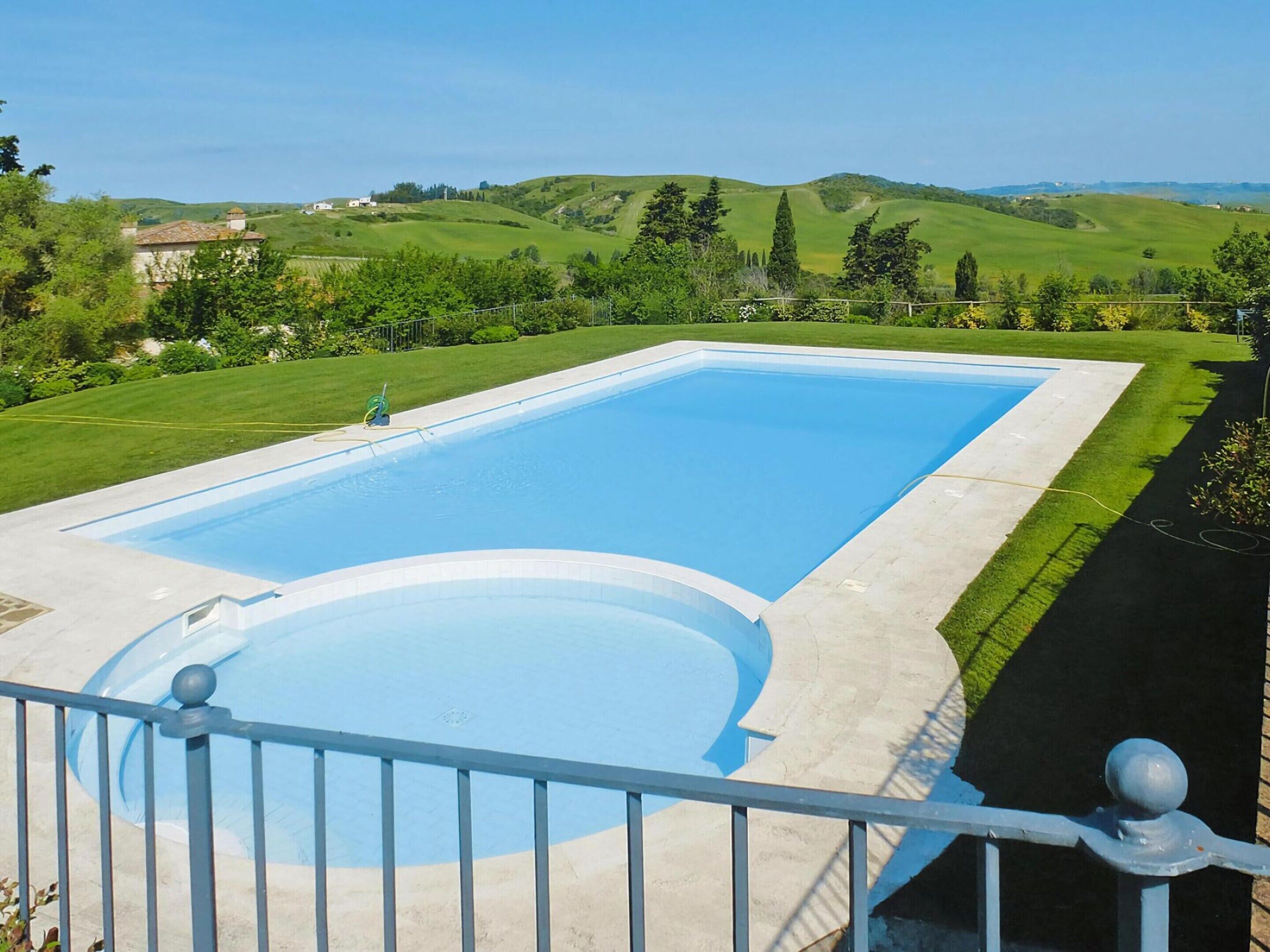 A rectangular swimming pool with a surrounding deck, set against a backdrop of rolling hills and greenery.