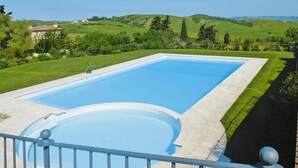 Une piscine rectangulaire entourée d’une terrasse, avec en arrière-plan des collines verdoyantes.