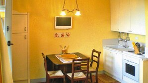 Une cuisine compacte comprenant une table à manger, des chaises, un petit téléviseur et les appareils électroménagers de base.