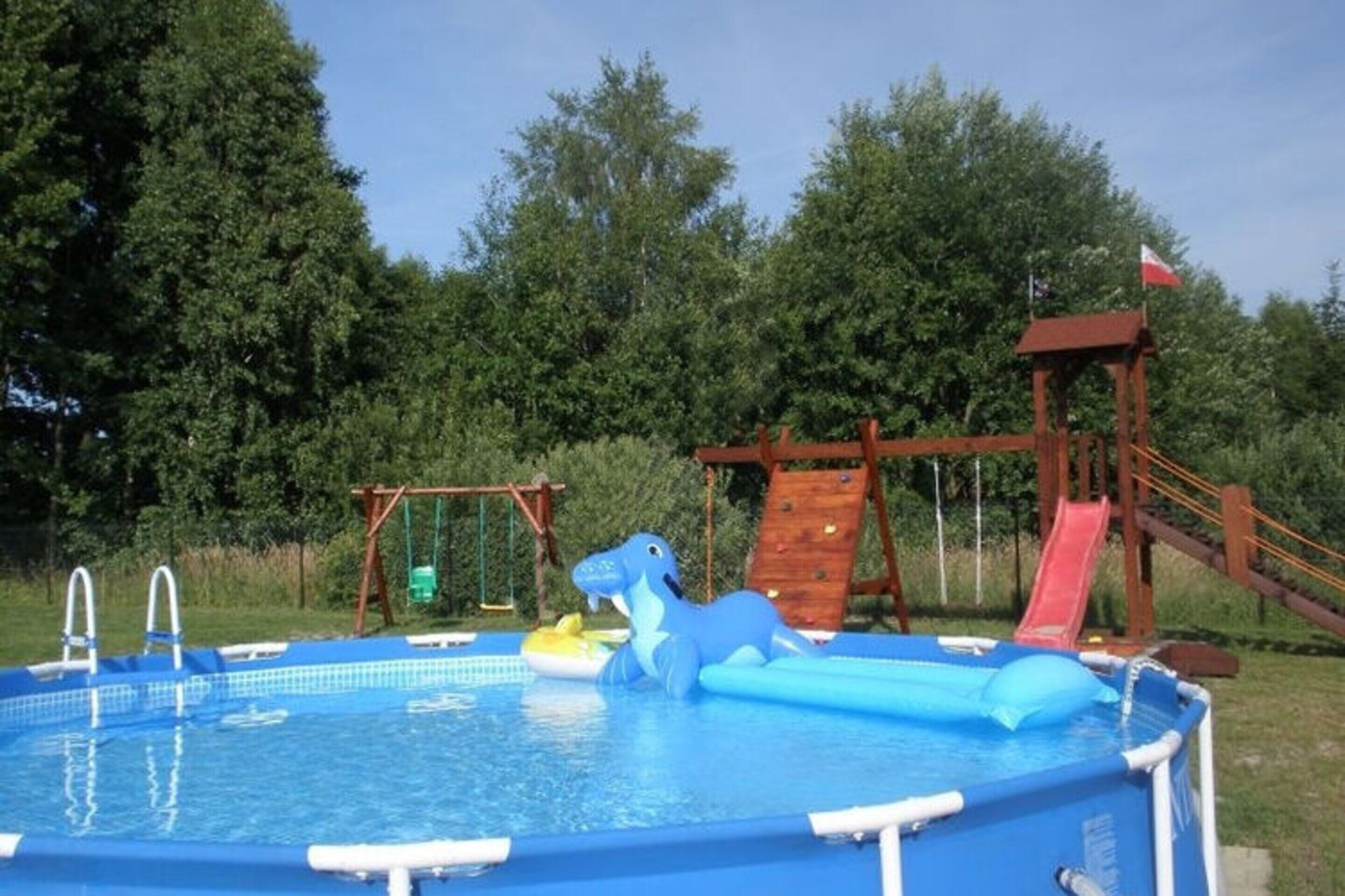 An outdoor swimming pool with a slide and a wooden play structure.