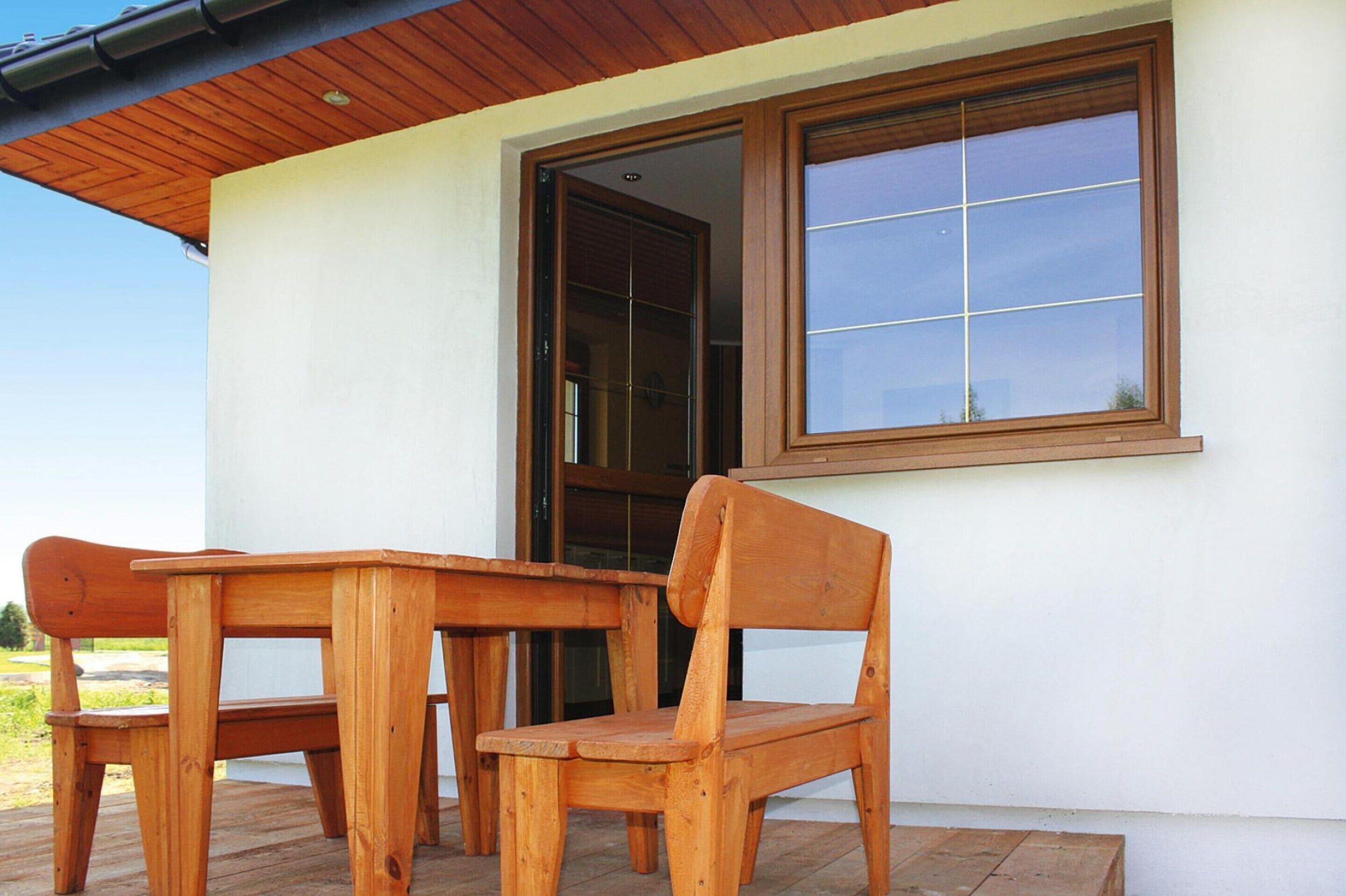 A wooden table and two chairs outside a building with a large window.