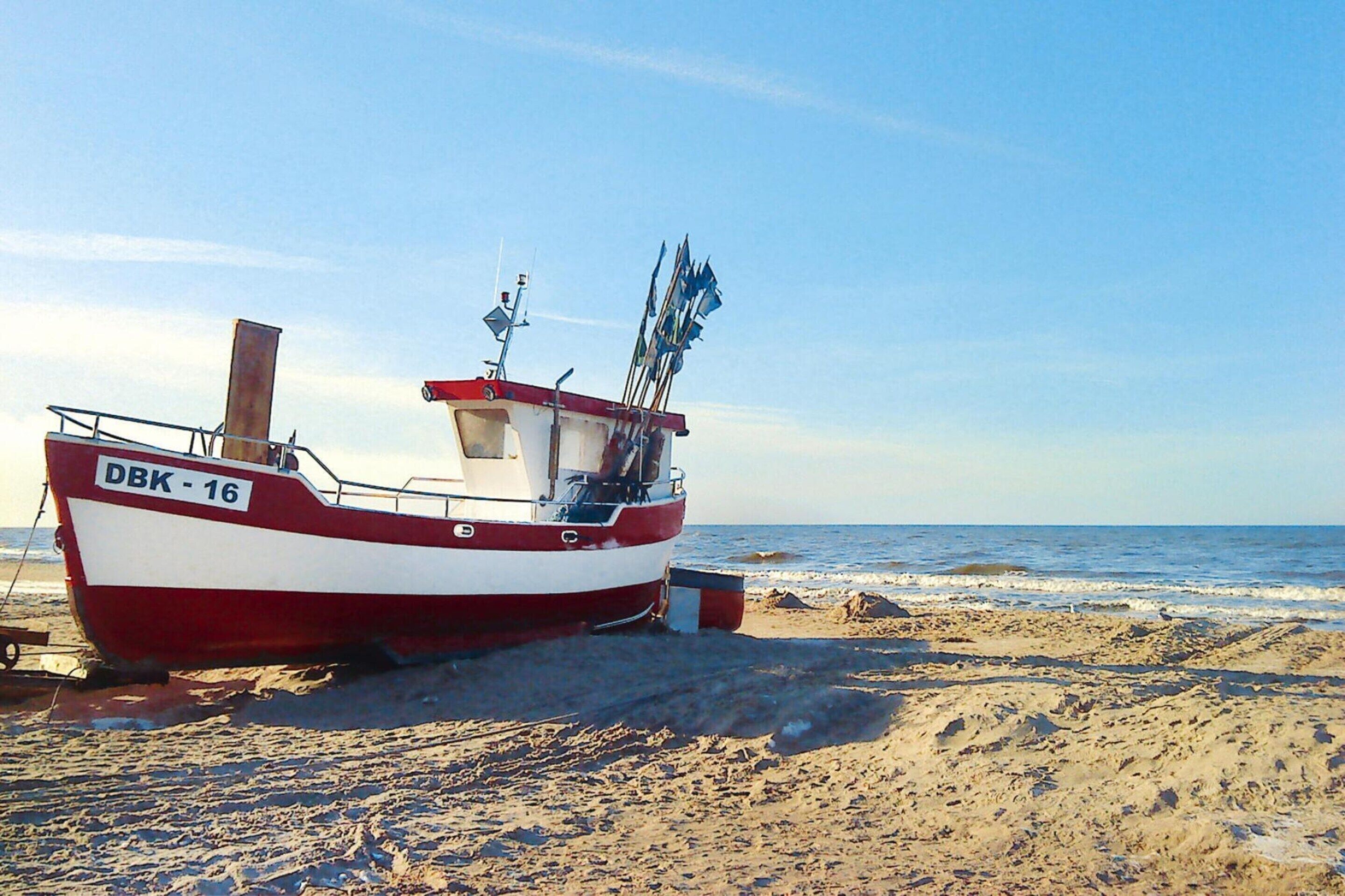 Una embarcación roja y blanca llamada DBK-16 en una playa arenosa cerca del agua.