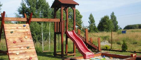 A wooden playground with a slide and climbing wall.
