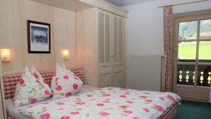 A bedroom with a bed, floral bedding, a wooden wardrobe, a framed picture on the wall, and a window with a view of greenery. - Apartment in Krimml With Parking Space (Krimml)