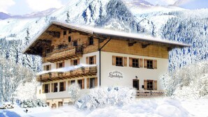 A two-story wooden building with a balcony, surrounded by snow-covered trees and mountains. - Apartment in Krimml With Parking Space (Krimml)