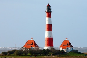 A tall lighthouse with a red and white striped tower, surrounded by two smaller buildings with red roofs. - Holiday Home in Busum in a Beautiful Area (Büsum)