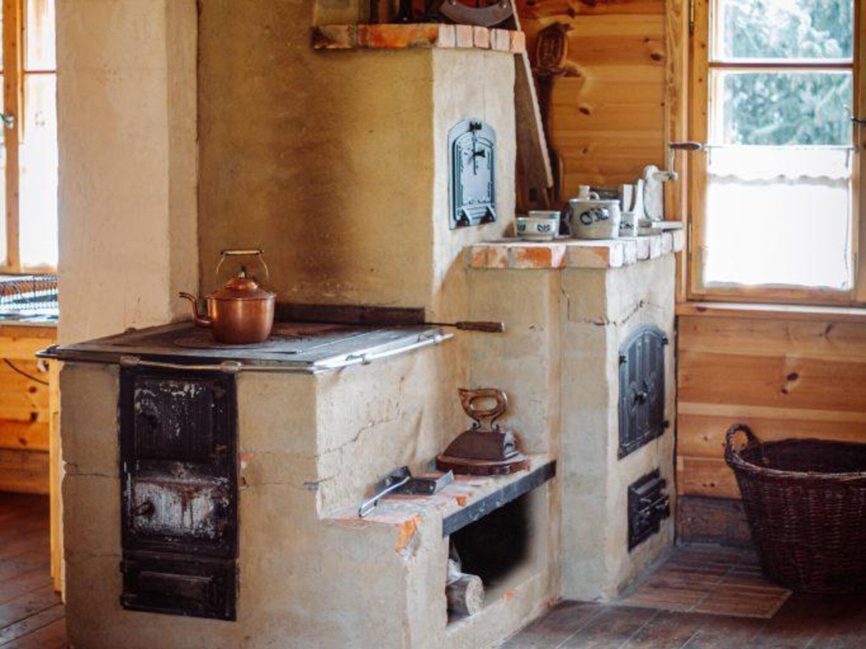 A rustic wooden cabin interior with a wood-burning stove, a window with a view of trees, and a wooden floor.