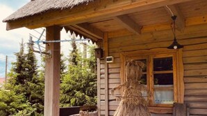 Una cabaña rústica de madera con techo de paja, un banco de madera afuera y una ventana con vistas al bosque circundante.