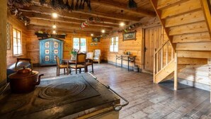 Interior rústico de una cabaña de madera con comedor, estufa de cocina y una escalera.