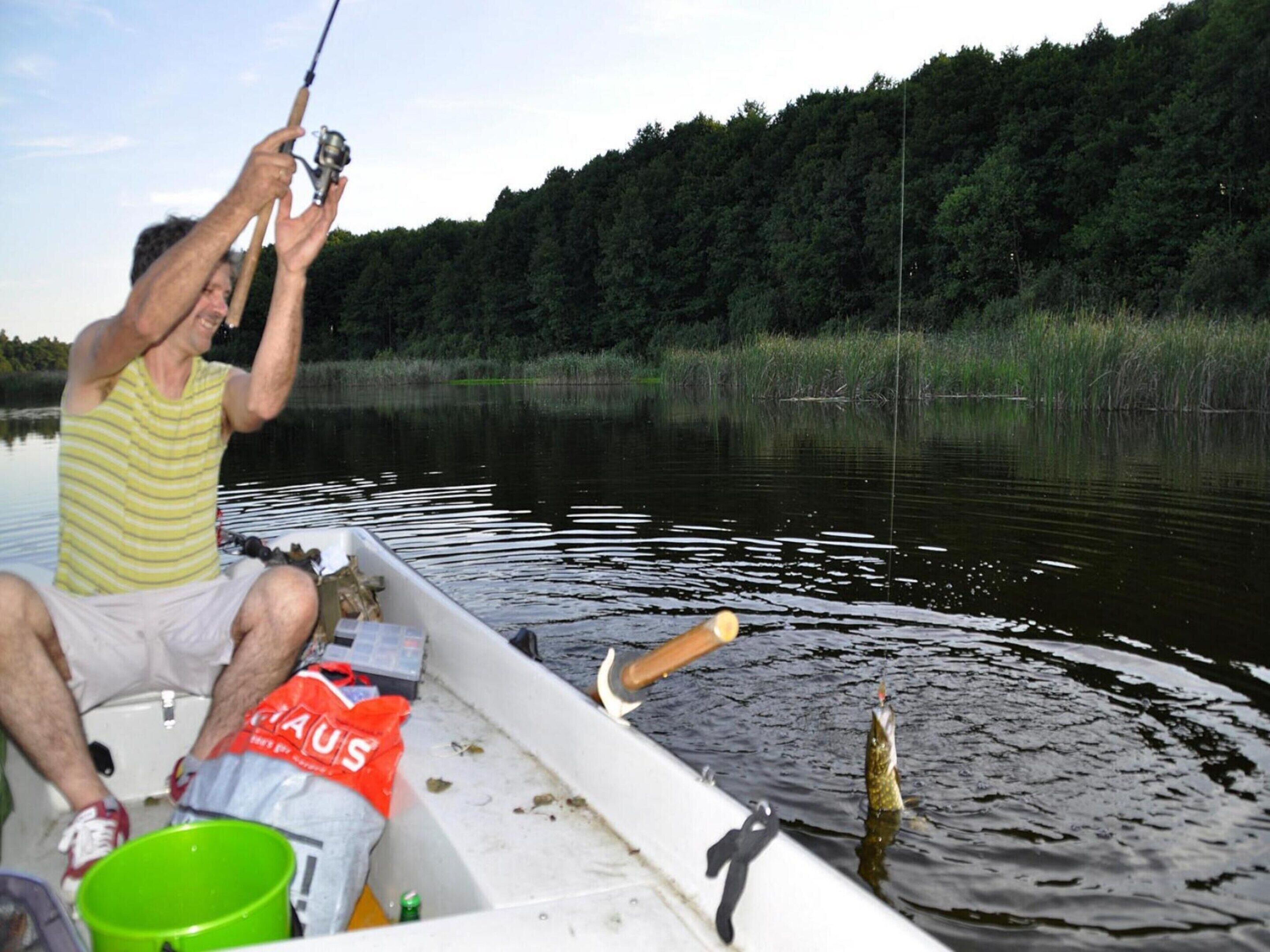 Une personne pêchant depuis un bateau sur un lac calme, avec une forêt dense en arrière-plan.