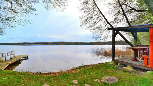 Un parque junto al lago con un muelle de madera, mesas de picnic y una zona de estar techada.