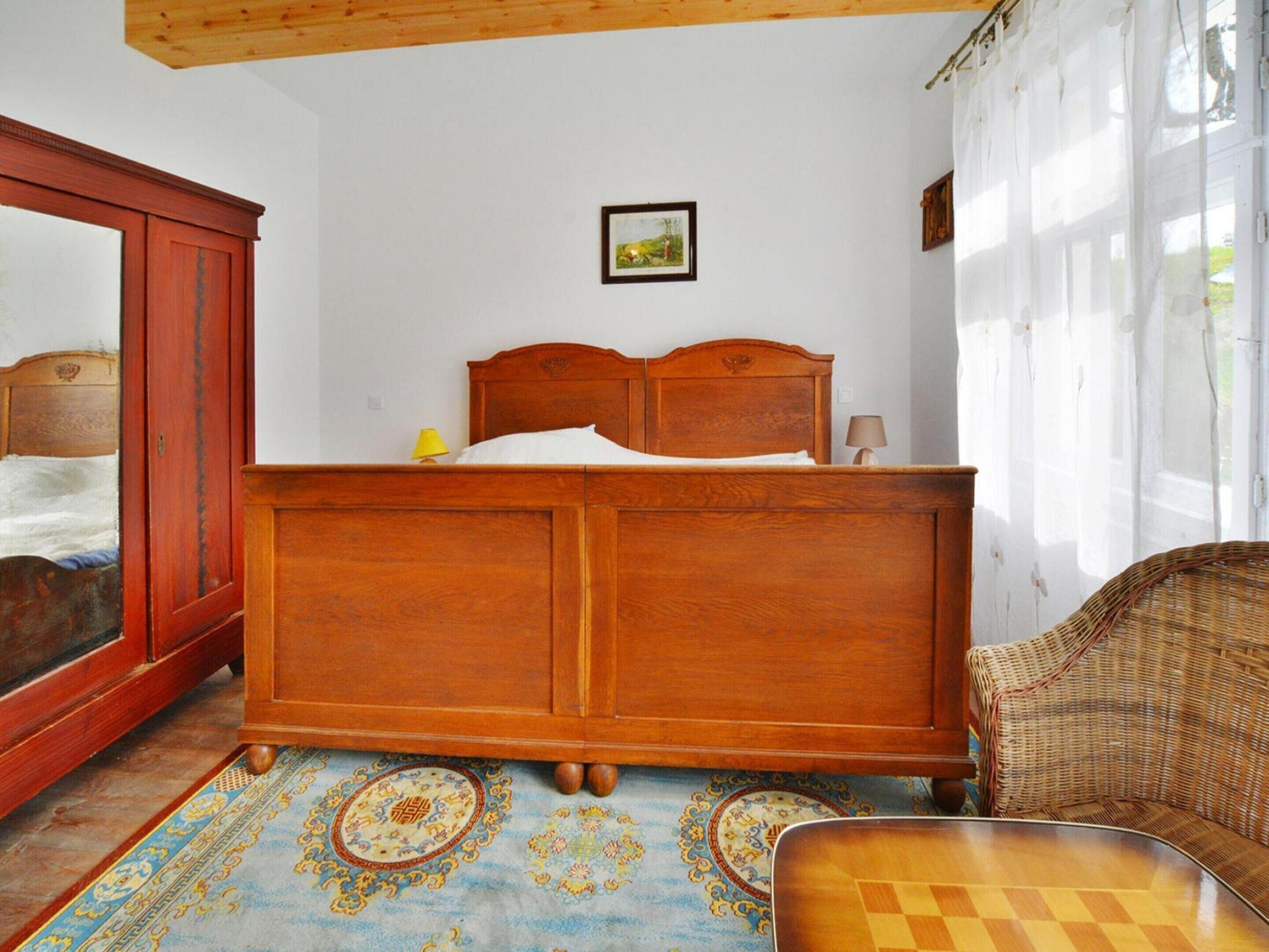 A bedroom with a wooden bed, a wicker chair, a large mirror, and a patterned rug.