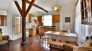 Amplia sala de estar con una mesa de comedor de madera, sillas y un banco. Se ve una cocina con armarios de madera y una ventana al fondo.