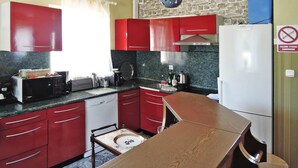 Una cucina compatta con mobili rossi, un frigorifero bianco Bosch, un tavolo in legno e una parete in pietra.