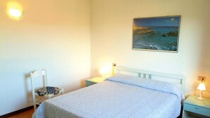 Un dormitorio con cama, una silla, una mesita de noche y una lámpara de pared.