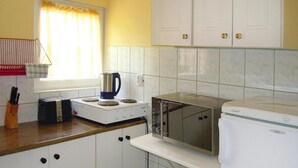 Una cocina compacta con armarios blancos, un tostador, una tetera, un microondas y un refrigerador.