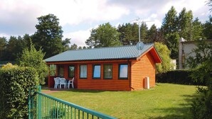 Una pequeña cabaña de madera con techo de tejas, un patio cercado y un pequeño porche con sillas.