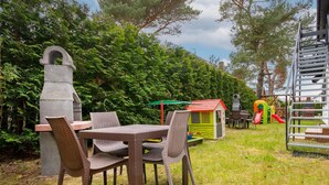 A patio with wicker chairs and a stone table, a children's playhouse, and a slide in the background. - Apartment in Jaroslawiec Near the Beach (Postomino)