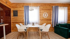 A wooden-paneled room with a dining table, white chairs, a green sofa, and a ship's wheel decoration. - Apartment in Jaroslawiec Near the Beach (Postomino)