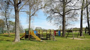 A playground with various play structures including a slide and swings, surrounded by trees and grassy area. - Holiday Home in Stepnica for 6 Persons (Stepnica)