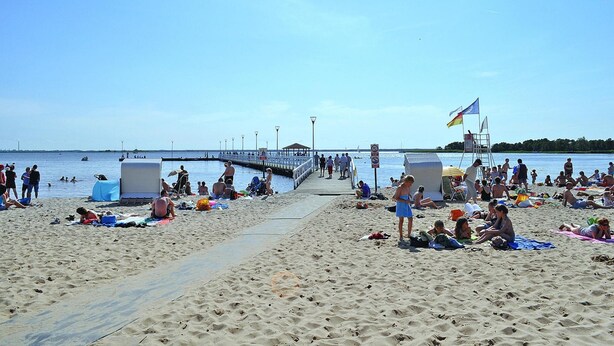 A beach with a pier extending into the water, people sunbathing and swimming, and a lifeguard tower. - Holiday Home in Stepnica for 6 Persons (Stepnica)
