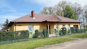 A yellow building with a brown roof, surrounded by a green fence. - Holiday Home in Stepnica for 6 Persons (Stepnica)