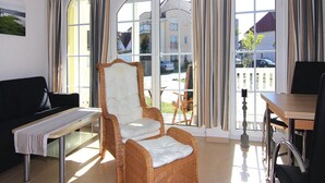 A room with a wicker chair, a black sofa, a wooden table, and a bench. - Ferienwohnung, Graal-muritz (Graal Mueritz)