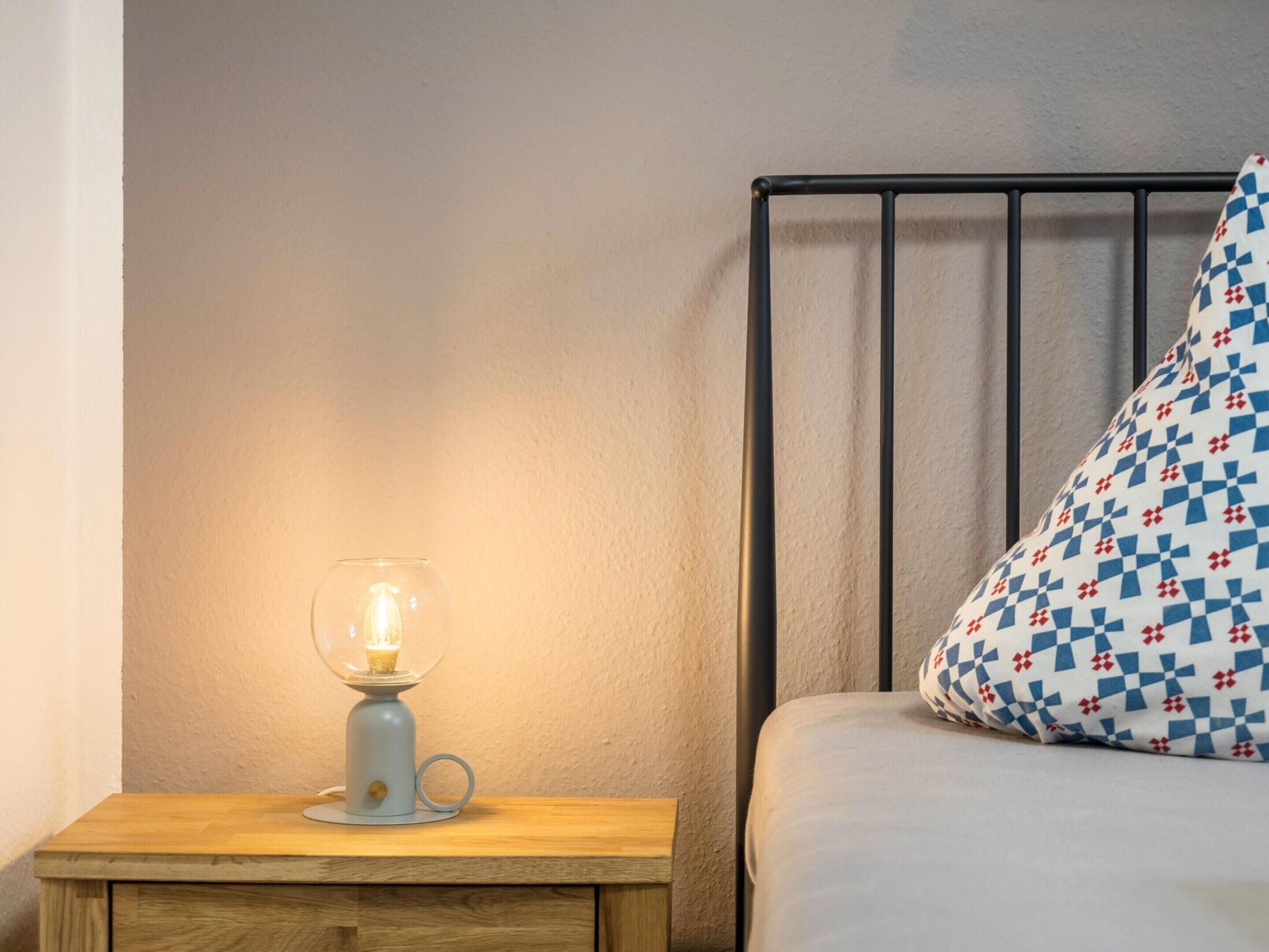A bed with a patterned pillow and a bedside table with a lamp.