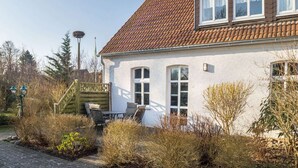 A two-story house with a tiled roof, a front porch with a table and chairs, and a wooden fence. - Lichtdurchflutete Ferienwohnung in Buchholz am Muritzsee (Buchholz)