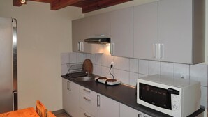 Une cuisine compacte avec des meubles blancs, un four à micro-ondes, une bouilloire et une table en bois.