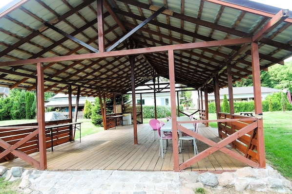 A covered outdoor area with a wooden deck, stone pathway, and seating arrangements.