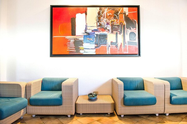 Un hall con tres sillones de mimbre con cojines verde azulado, una pequeña mesa redonda con un cuenco y un cuadro abstracto grande en la pared.