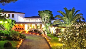 A well-lit residential property with a paved driveway, a large cactus, and various flowering plants. - Residence Cormoran, Loc. Campus Villasimius (Villasimius)