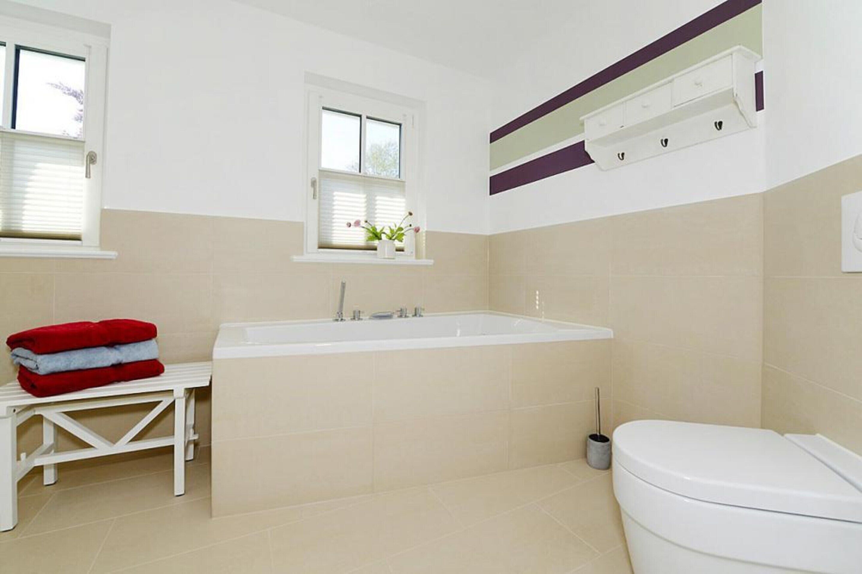 A bathroom with a bathtub, toilet, and a bench with towels.