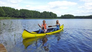 Two people in a yellow canoe on a calm lake with a dock in the foreground and a forested shoreline in the background. - Great Holiday Home in the Middle of Nature and Right on the Lake, Natac Wielka (Nidzica)