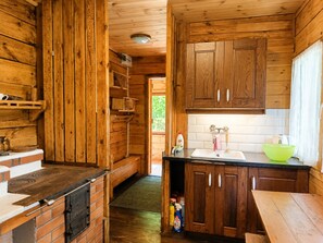 A wooden cabin interior with a kitchen area, including a stove, sink, and cabinets. - Holiday Home Right on the Lake, Natac Wielka (Nidzica)
