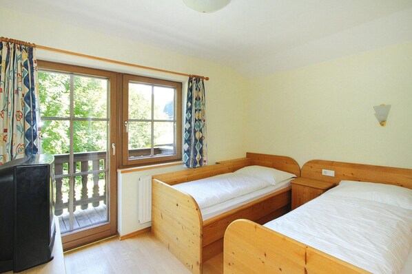 A room with two wooden beds, a window with curtains, a radiator, and a television.