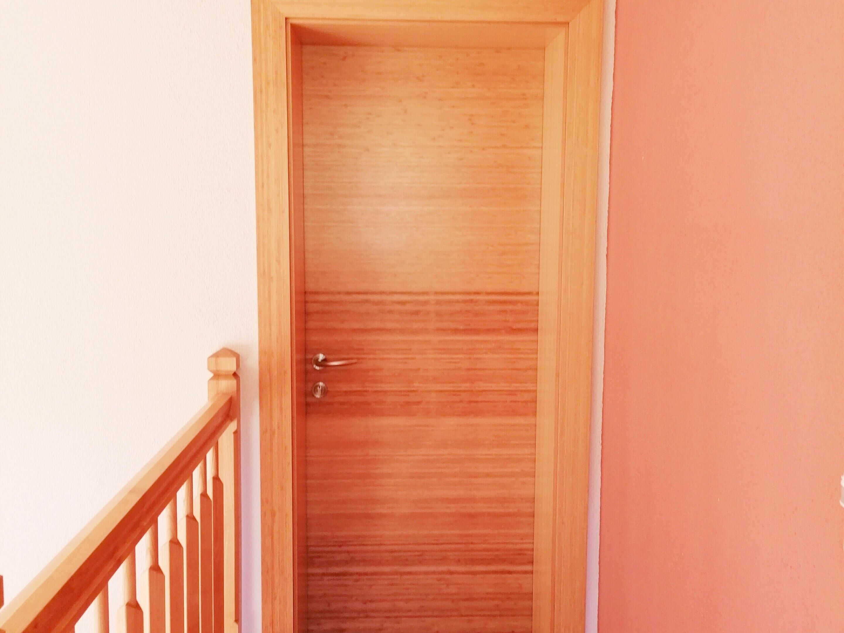 Une porte en bois, dotée d’une poignée et d’un trou de serrure, qui donne sur une pièce avec un mur blanc et une rambarde en bois.