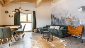 Una sala de estar acogedora con techo de madera, un sofá verde, una mesa de comedor con sillas y un tapete de cuero de vaca.