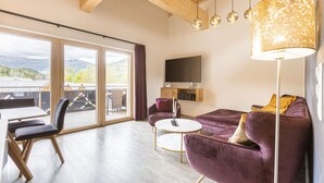 Ein geräumiges Wohnzimmer mit großem Fenster, einer Couch, einem Couchtisch und einem Flachbildfernseher.